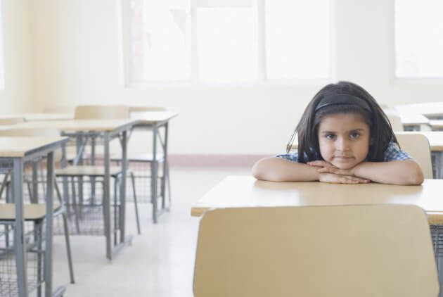 Portrait of a schoolgirl leaning on a desk in a classroom